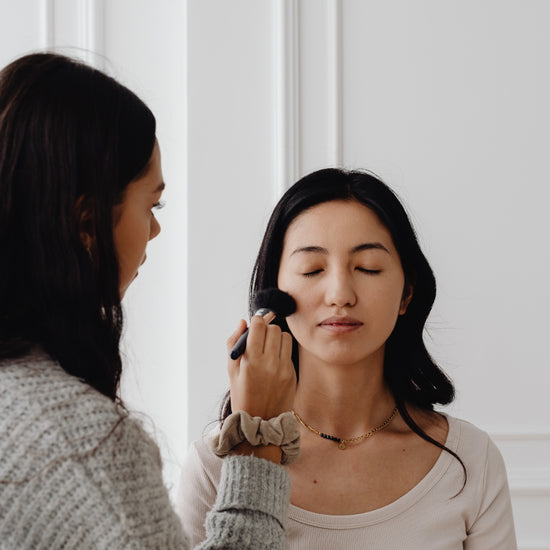Woman applying makeup to another woman's face with a brush.